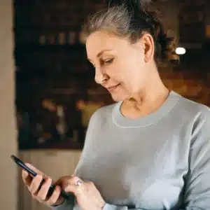 Middle Age Woman In Grey Sweater Looks Down At Phone