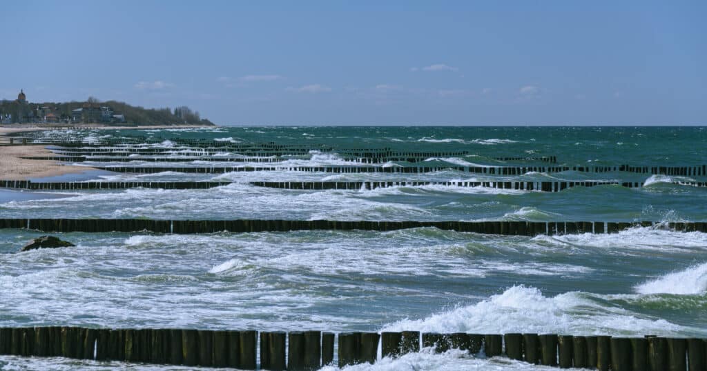 Ocean groins extend into ocean from sand beach while waves come to shore with whitecaps